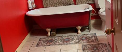 Un bagno con una vasca da bagno rossa, un water e un lavandino. Si nota una tenda decorata e un tappeto sul pavimento.