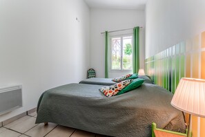 Une chambre à coucher avec un lit, une fenêtre avec des rideaux verts, un radiateur et une lampe.