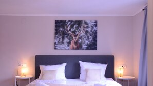 A neatly made double bed with white linens and pillows, two bedside tables with lamps, and a framed deer picture on the wall. - Beim Patzelt - Holiday home Nesselwang | Königscard | Pets welcome (Nesselwang)