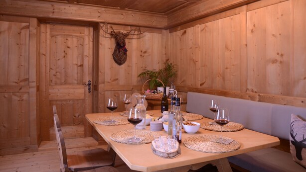 A wooden dining room with a long table set for a meal, featuring woven placemats, wine glasses, and a deer head decoration. - Beim Patzelt - Holiday home Nesselwang | Königscard | Pets welcome (Nesselwang)