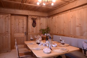 Una sala menjador de fusta amb una taula llarga preparada per a dinar, amb sotsamassos teixits, gots de vi i una decoració de cap de cérvol.