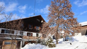 A wooden chalet with a balcony, surrounded by snow and leafless trees. - Beim Patzelt - Holiday home Nesselwang | Königscard | Pets welcome (Nesselwang)