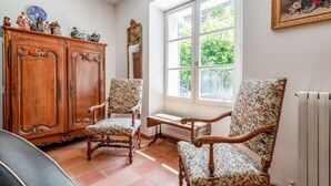 A room with two wooden chairs with floral upholstery, a wooden cabinet with figurines, and a large window with a view of greenery. - Villa 'Le Mas' with Mountain View, Private Pool and Wi-Fi (Entrechaux)