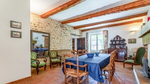 A dining area with a stone wall, wooden beams, and a table set for four. - Villa 'Le Mas' with Mountain View, Private Pool and Wi-Fi (Entrechaux)