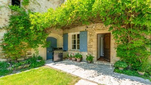 A stone building with a garden patio, a grill, and potted plants. - Villa 'Le Mas' with Mountain View, Private Pool and Wi-Fi (Entrechaux)