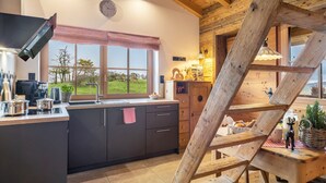 A kitchen with a large island, wooden beams, a window with a view, and a staircase.