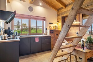 A kitchen with a large island, wooden beams, a window with a view, and a staircase.