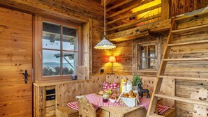 A wooden cabin interior with a dining table set for two, a bench, and a hanging light fixture.