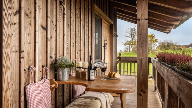 A wooden cabin with a wooden table, bench, and a bottle of wine.