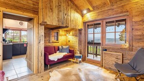 A wooden cabin interior with a sofa, a chair, a cowhide rug, and a kitchen area.