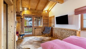 A log cabin room with a bed, a chair, a TV, and a window.