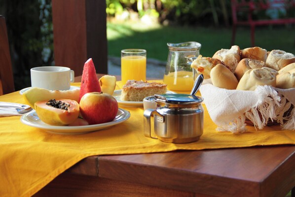 A breakfast table with fruits, bread, a coffee pot, and a glass of orange juice. - Pousada do Cais (Paraty)