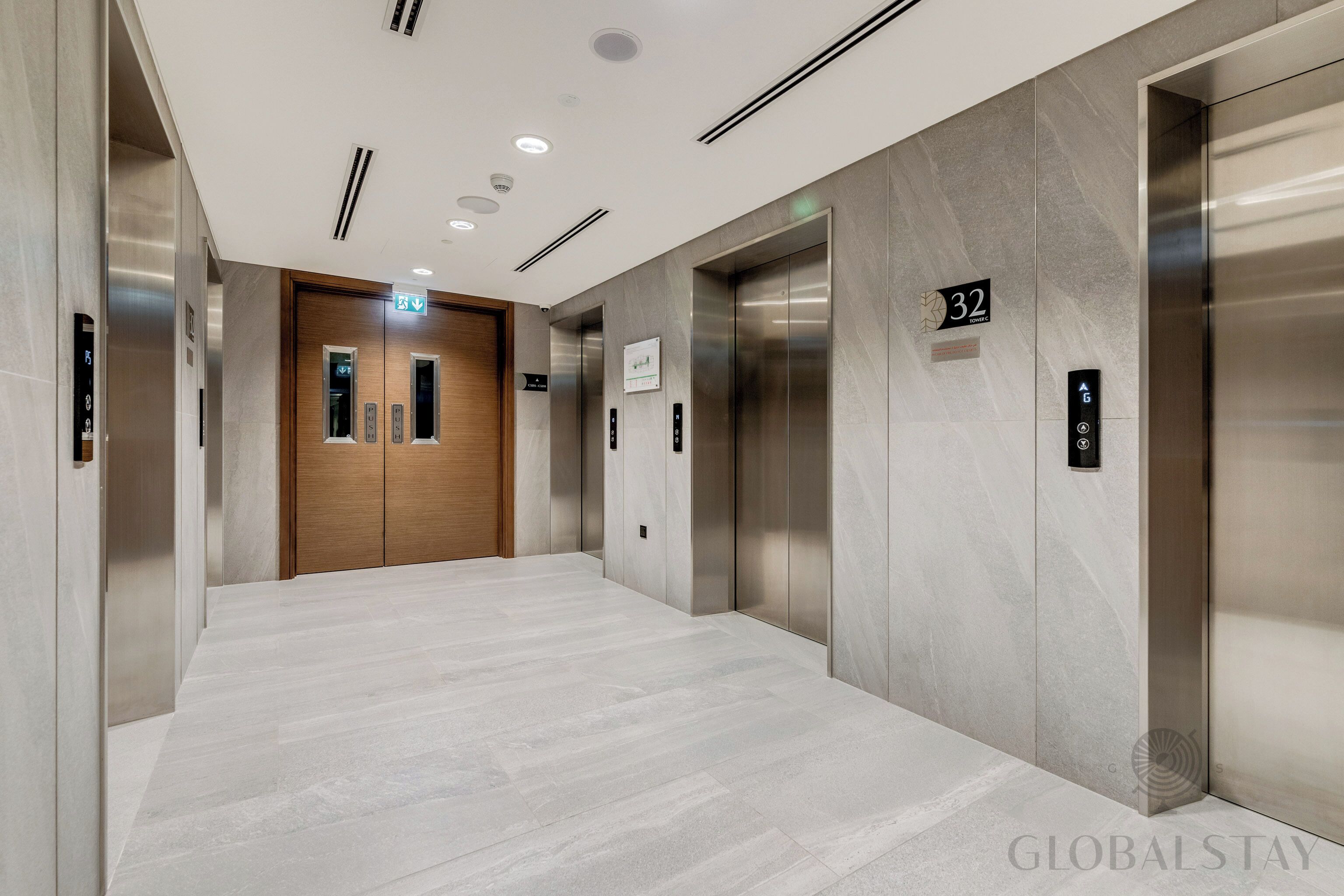 A modern elevator lobby with a marble floor, wooden door, and two elevators.