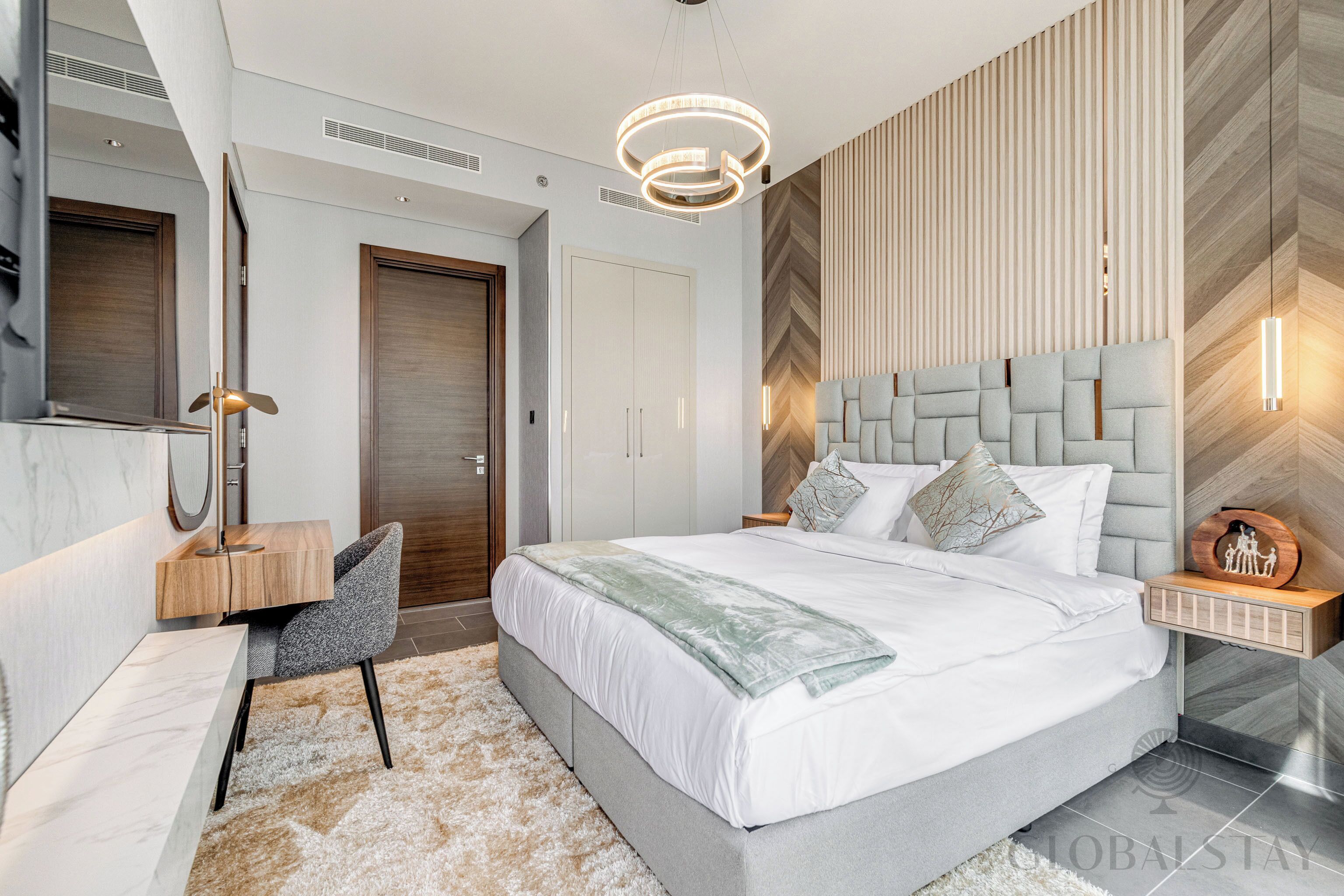 A modern bedroom with a large bed, a desk, a chair, and a wardrobe.
