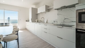 Een moderne keuken met witte kasten, een marmeren spatwand en een groot raam met uitzicht op een balkon.