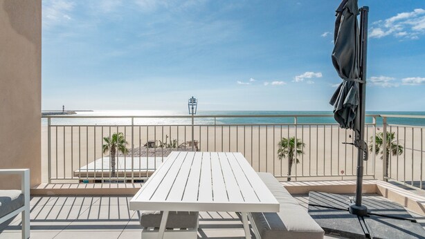 Een balkon met een tafel en stoelen, uitzicht op het strand en een palmboom.