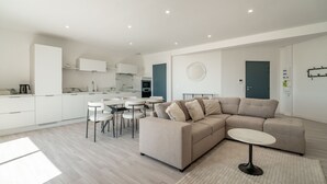 Een moderne woonkamer met een modulaire bank, een ronde salontafel en een eethoek met witte stoelen.