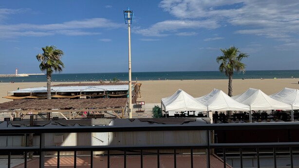 A beach view with tents, palm trees, and a lighthouse in the distance. - Holiday Home 'Face À La Mer 2' with Private Terrace and Air Conditioning (Port la nouvelle)