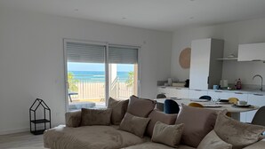 A modern living room with a large beige sectional sofa, a round coffee table, and a view of the beach through a sliding glass door. - Holiday Home 'Face À La Mer 2' with Private Terrace and Air Conditioning (Port la nouvelle)