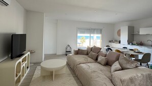 A modern living room with a large sofa, a TV, and a dining area with a kitchen in the background. - Holiday Home 'Face À La Mer 2' with Private Terrace and Air Conditioning (Port la nouvelle)