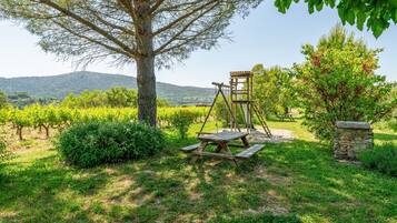 A picnic area with a wooden table and benches, surrounded by greenery and a stone wall.