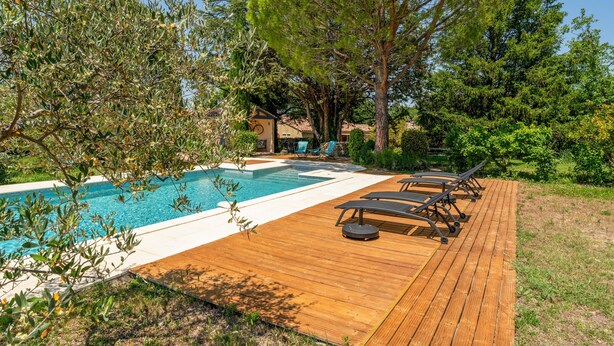 Ett trädäck med en pool, solstolar och ett hus i bakgrunden.