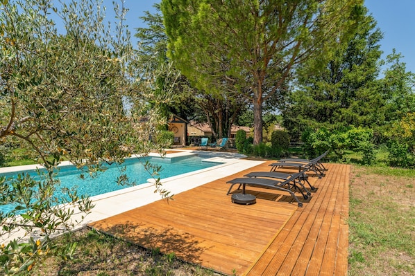 Une terrasse en bois avec une piscine, des chaises longues et une maison en arriĂšre-plan.