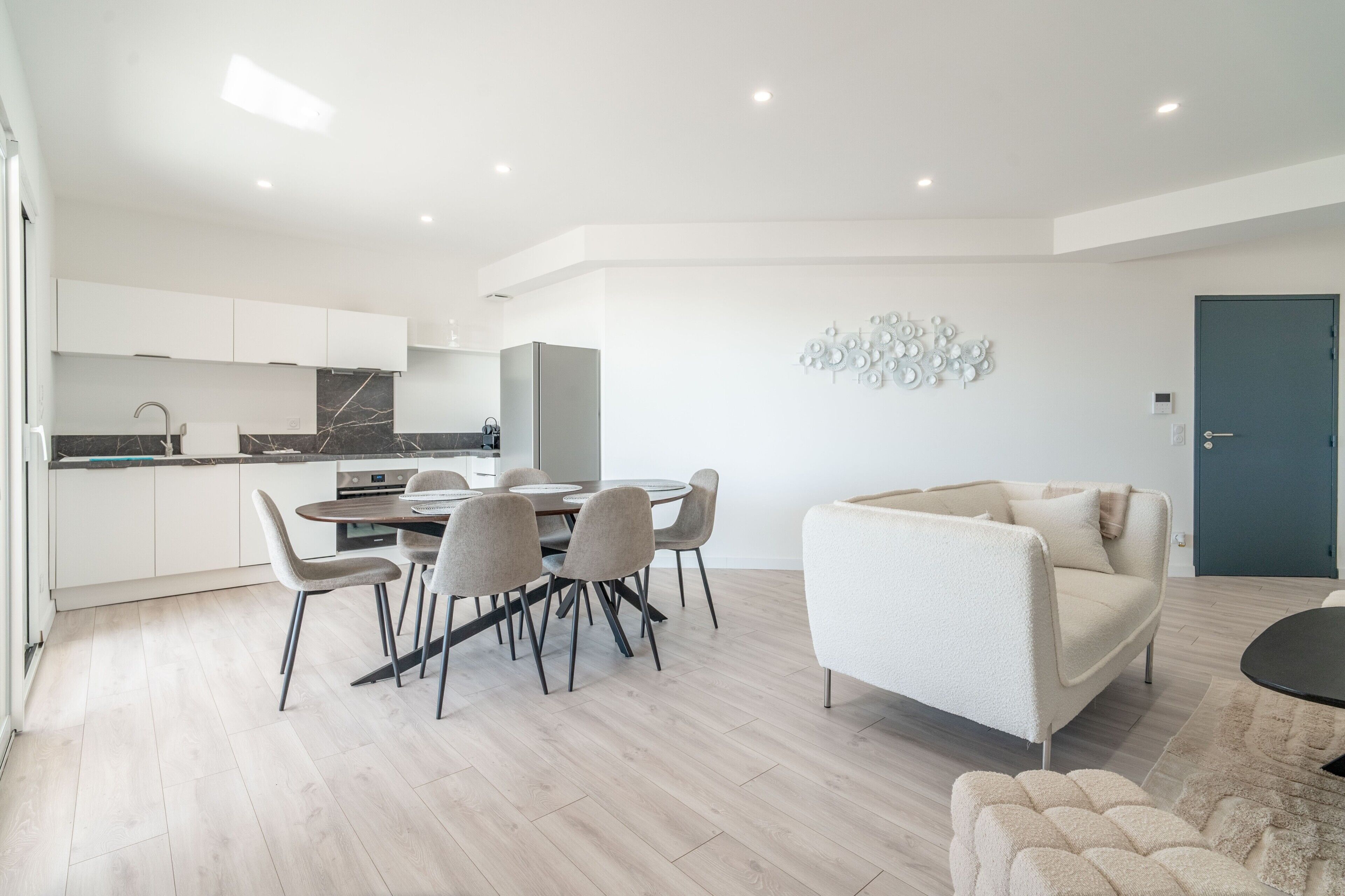 Een moderne woonkamer met een bank, een eettafel met stoelen, en een keuken met kasten en een koelkast.