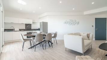 Een moderne woonkamer met een bank, een eettafel met stoelen, en een keuken met kasten en een koelkast.