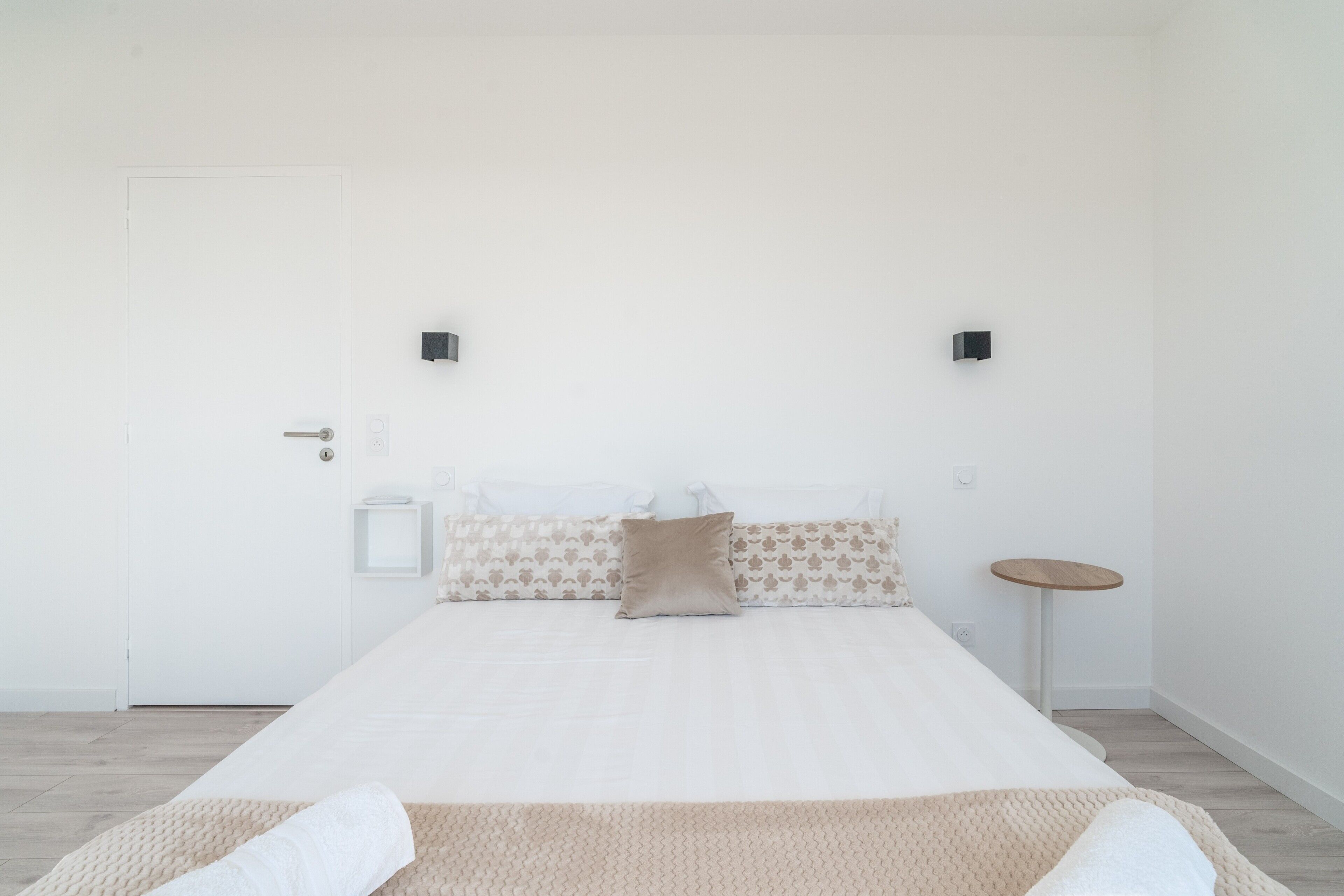 Une chambre à coucher au style minimaliste, avec un lit, des oreillers, une table de chevet et des lampes fixées au mur.