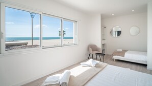 A bedroom with a large window, a bed, a chair, and a small table.