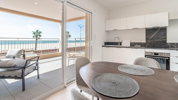 A modern kitchen with a marble countertop, a dining area with a table and chairs, and a balcony with a view of the sea.
