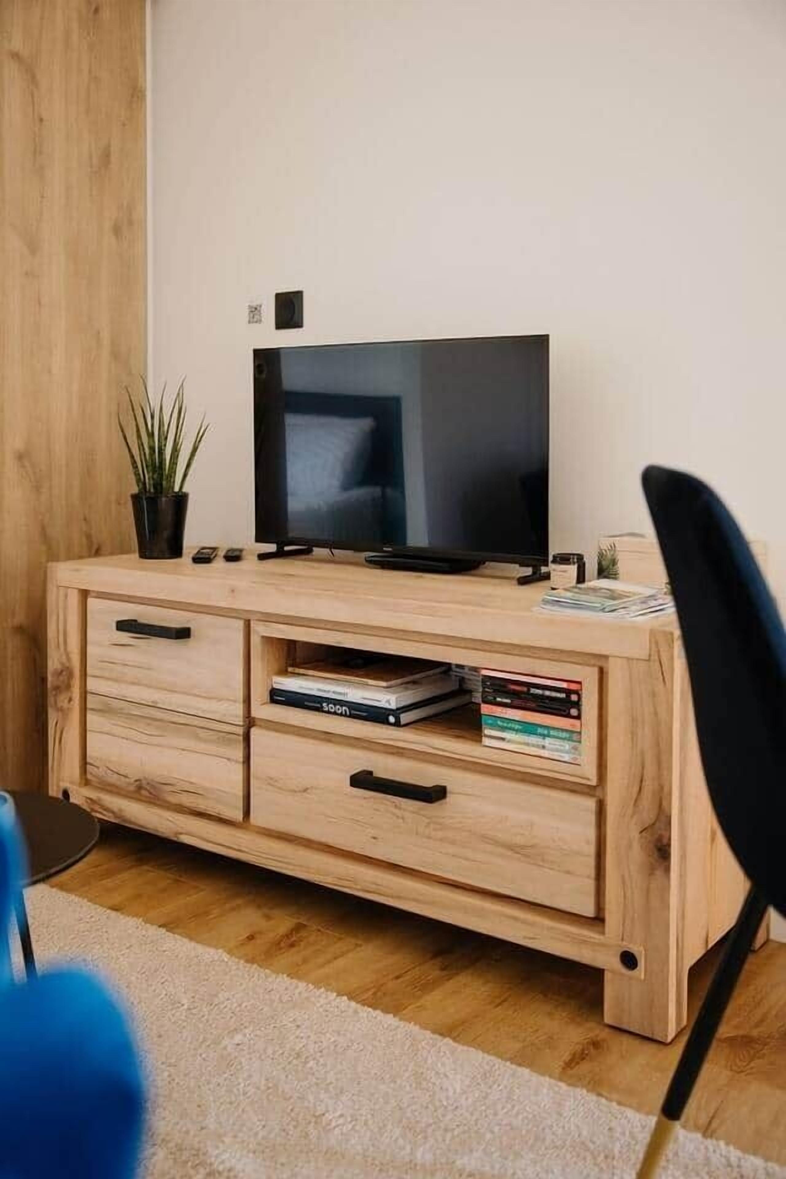 Ett TV-bord i trä med en platt-TV, några böcker och en liten växt.