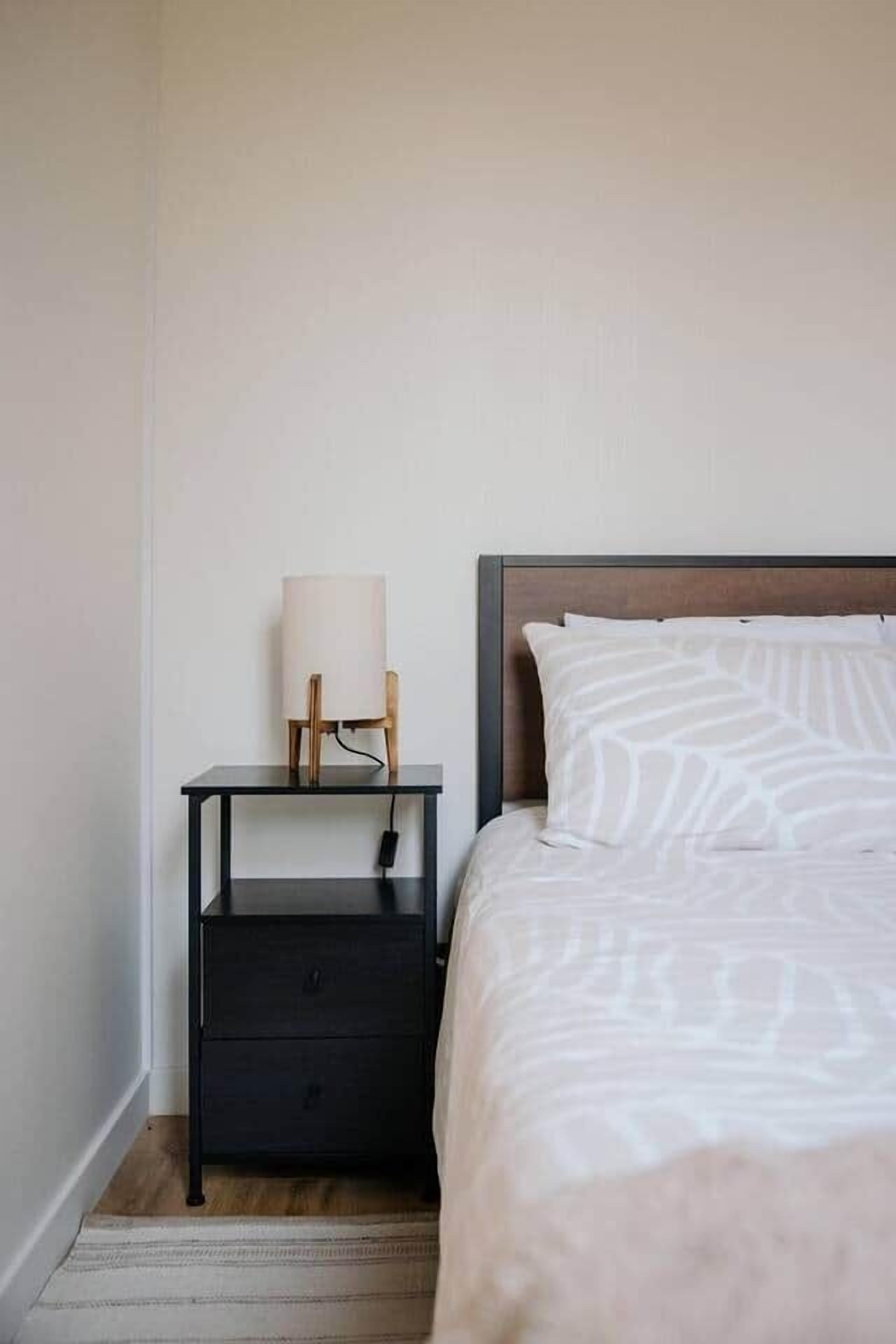A bedroom with a bed, a nightstand with a lamp, and a drawer.