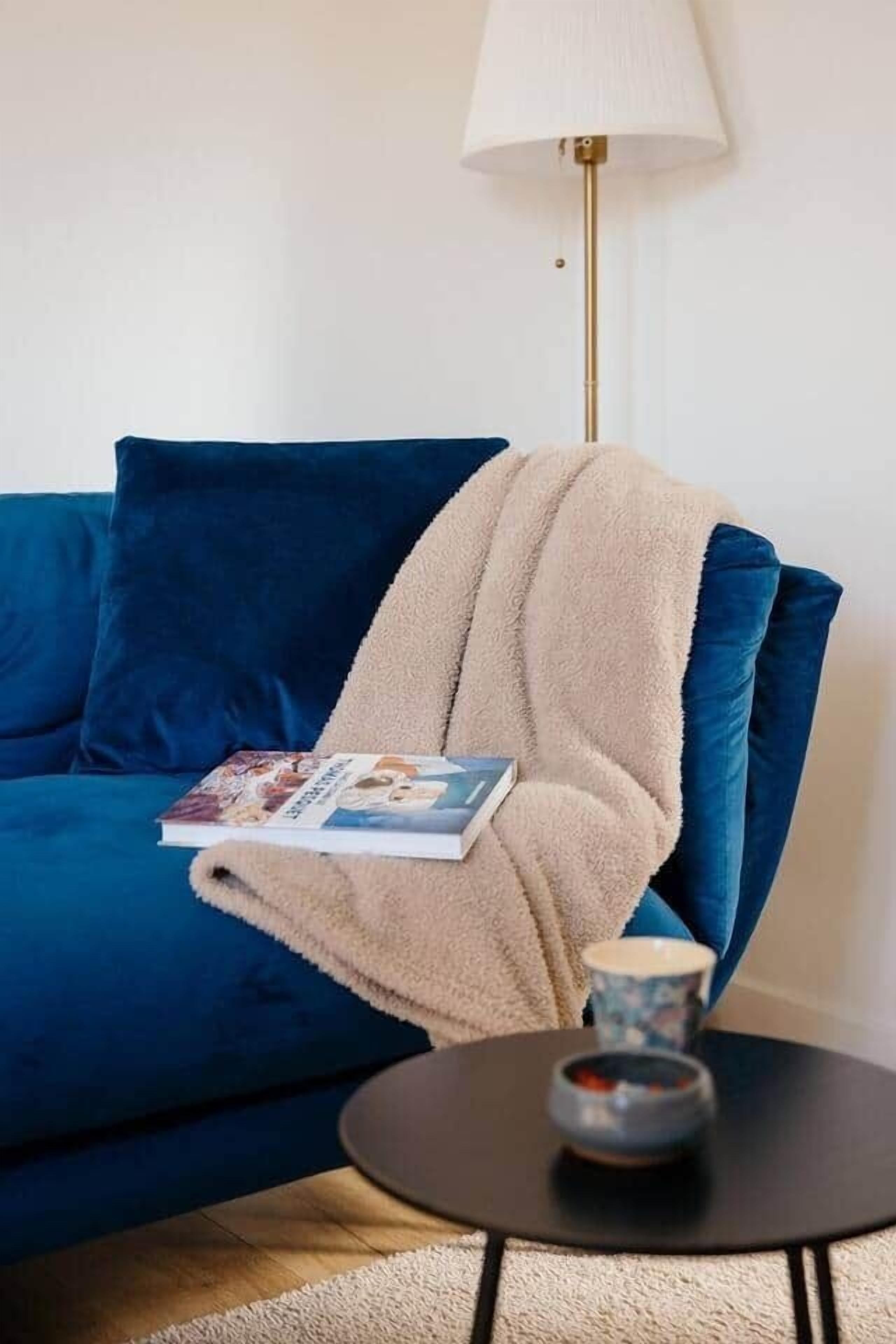 A blue sofa with a beige blanket, a book, and a small table with a cup and saucer.