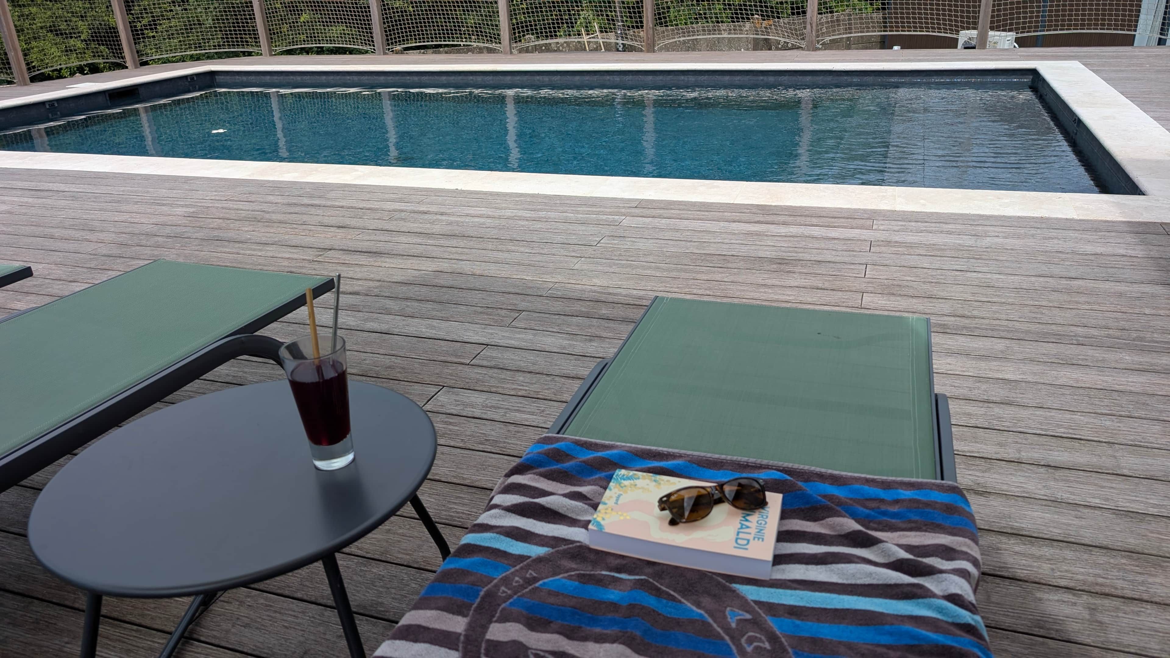 A poolside area with lounge chairs, a table, and a drink.