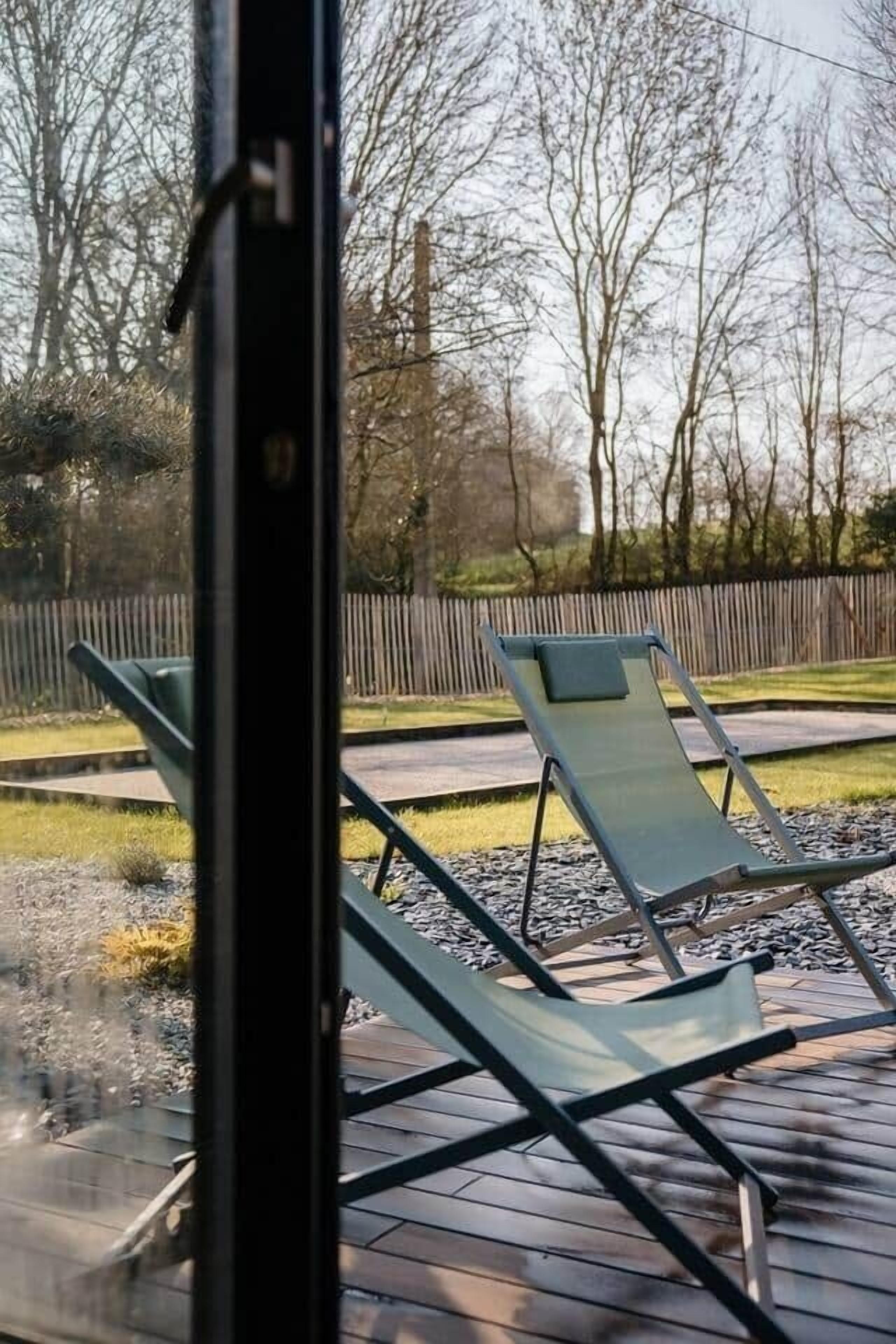 A deck with two lounge chairs and a wooden fence in the background.