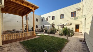 A courtyard with a wooden pergola, outdoor seating, and a small lawn. - Pakhlavon Boutique Hotel (Khiva)
