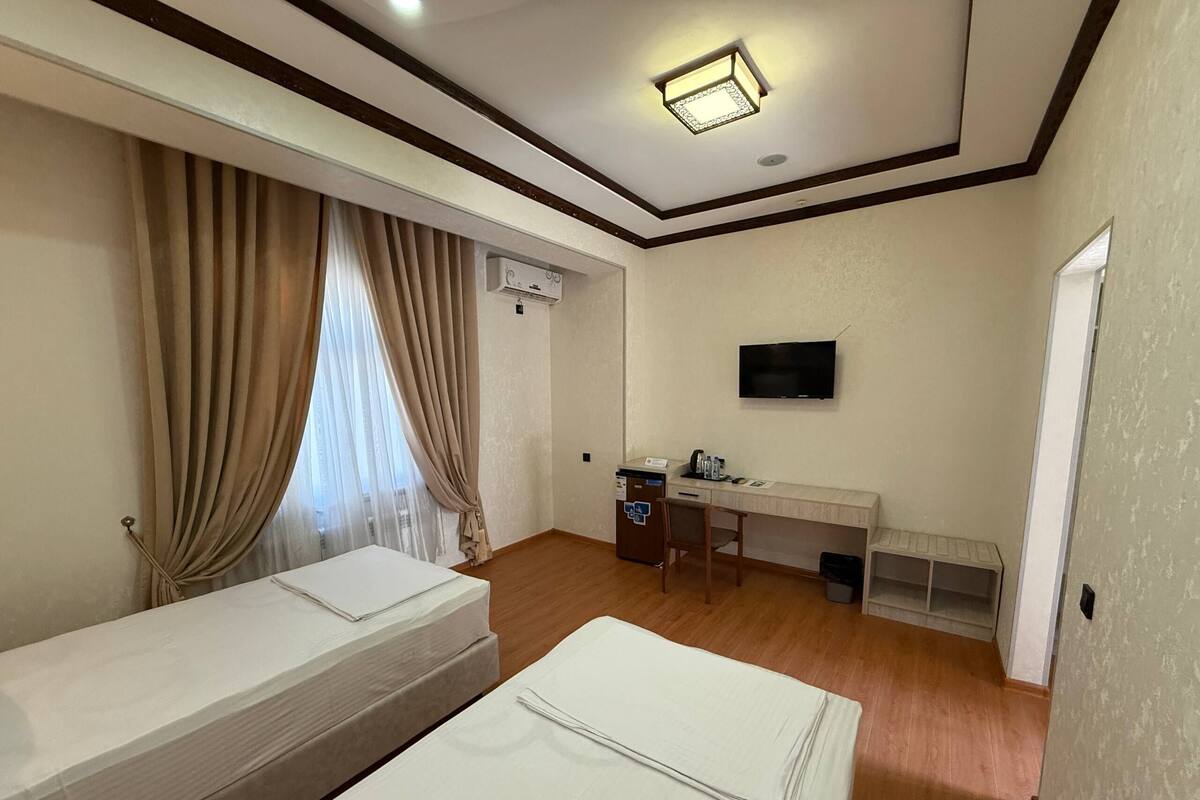 Une chambre d’hôtel avec deux lits, un bureau avec une chaise, un téléviseur fixé au mur et une fenêtre avec des rideaux.