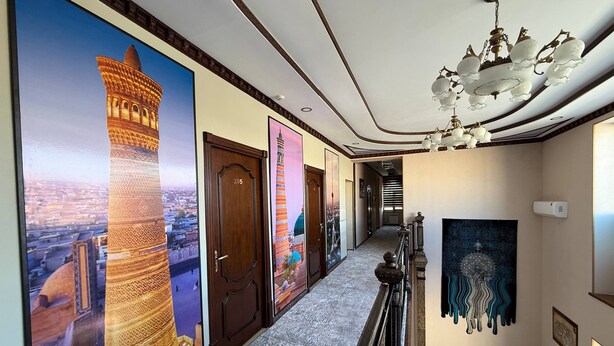 A hallway with a chandelier, a staircase, and a view of a cityscape through large windows. - Pakhlavon Boutique Hotel (Khiva)