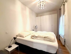 A bedroom with a bed, bedside table, lamp, ceiling fan, and wardrobe.