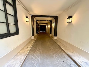 Un pasillo largo y estrecho con piso de baldosas y paredes a ambos lados. Hay dos luminarias empotradas en cada lado del pasillo.