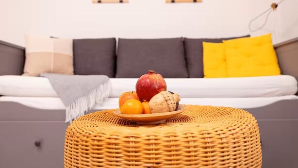 Ein Wohnzimmer mit einer Couch, einem runden Korbsessel und einer Obstschale auf dem Sessel.