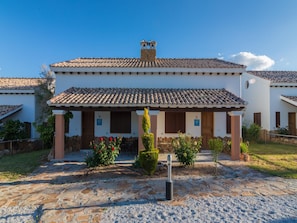 A white building with a tiled roof and a stone chimney. There are two doors with 'AT' signs, suggesting a restaurant or cafe.