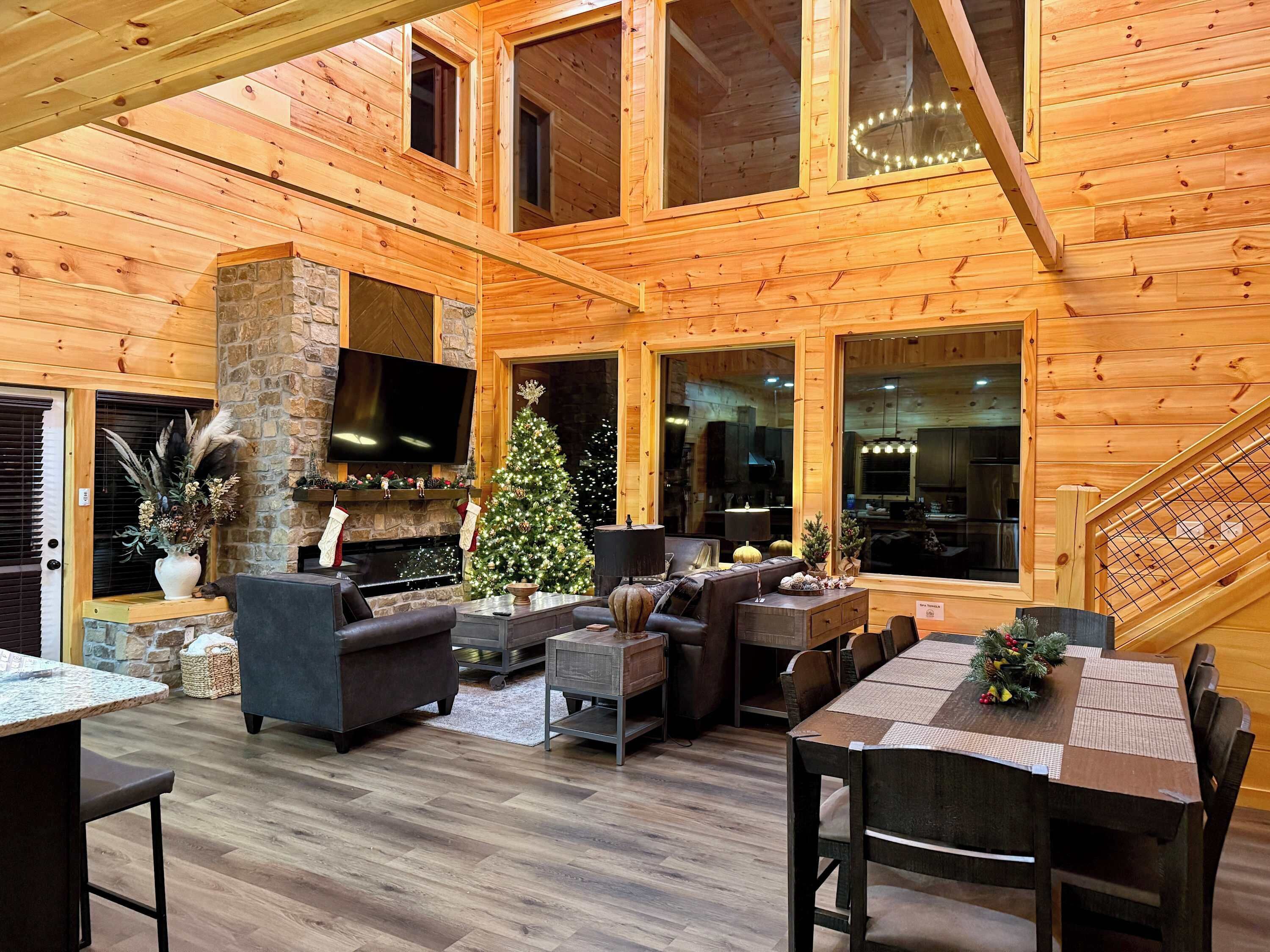 A cozy log cabin interior with a fireplace, a Christmas tree, and a dining area.
