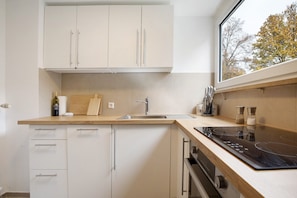 Une cuisine moderne avec des armoires blanches, un plan de travail en bois, une cuisinière encastrée et une fenêtre.