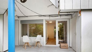 Una habitación con puerta de vidrio corredera, dos sillas blancas, una mesa pequeña y una caja de cartón en el suelo.