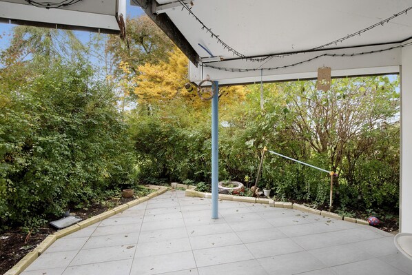 A covered outdoor area with a tiled floor, surrounded by dense greenery and trees.