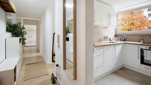 Una cocina moderna con armarios blancos, un ventanal con vista a árboles otoñales y un horno empotrado.