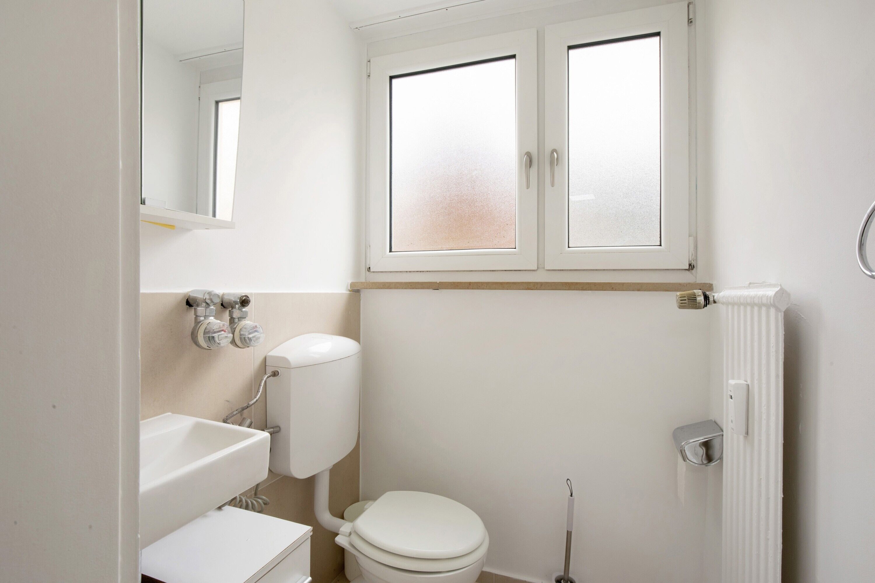 A bathroom with a toilet, sink, and window.